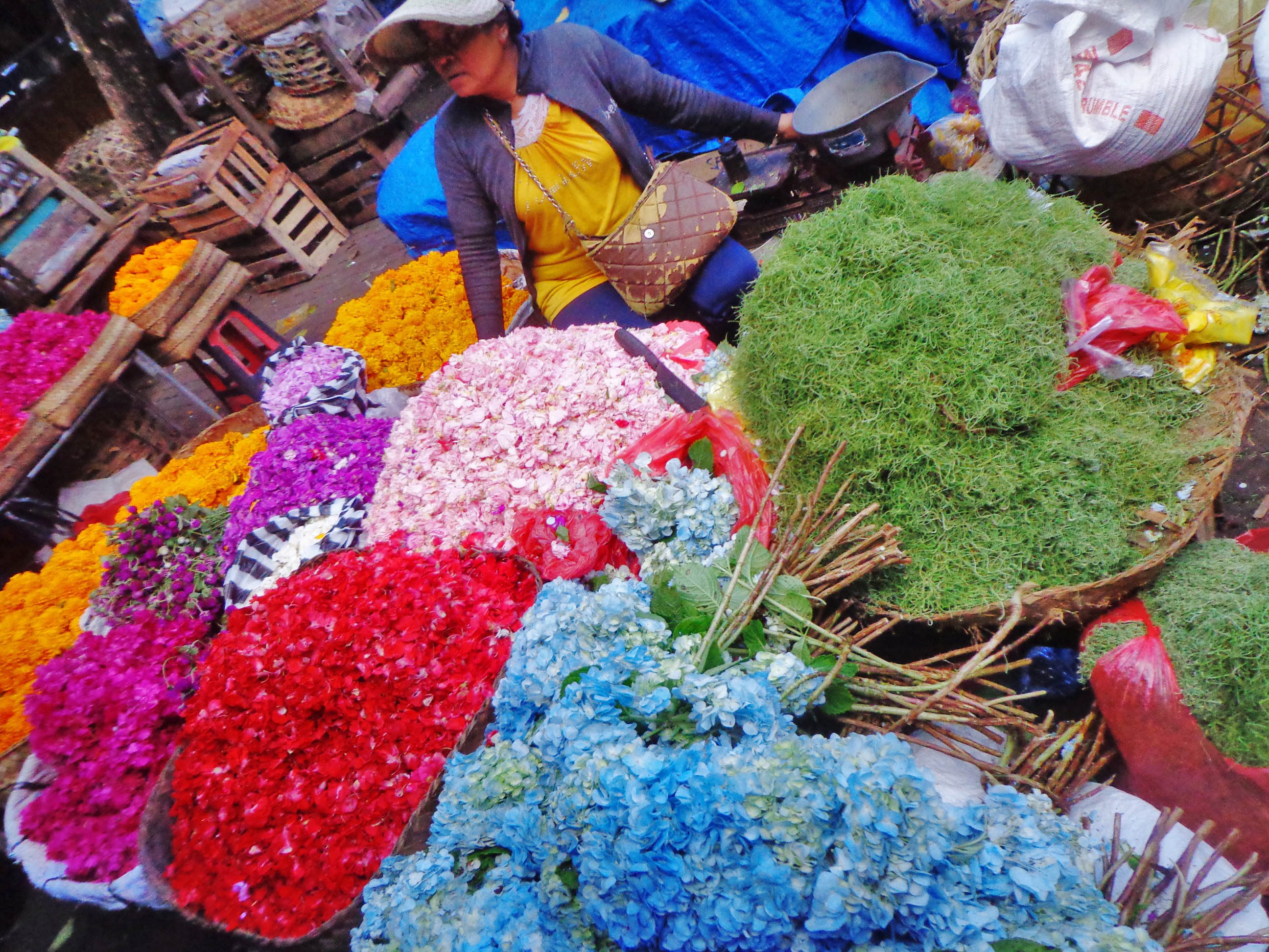 a woman sitting in a market with many colorful flowers