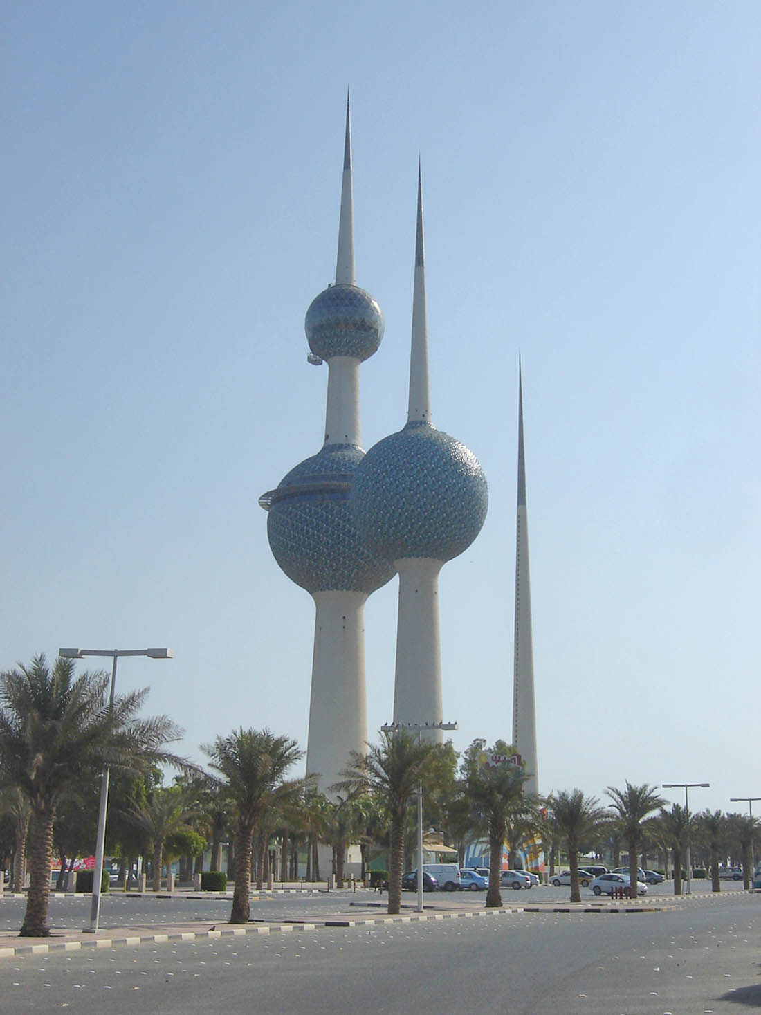 a tall towers with pointed towers and trees with Kuwait Towers in the background