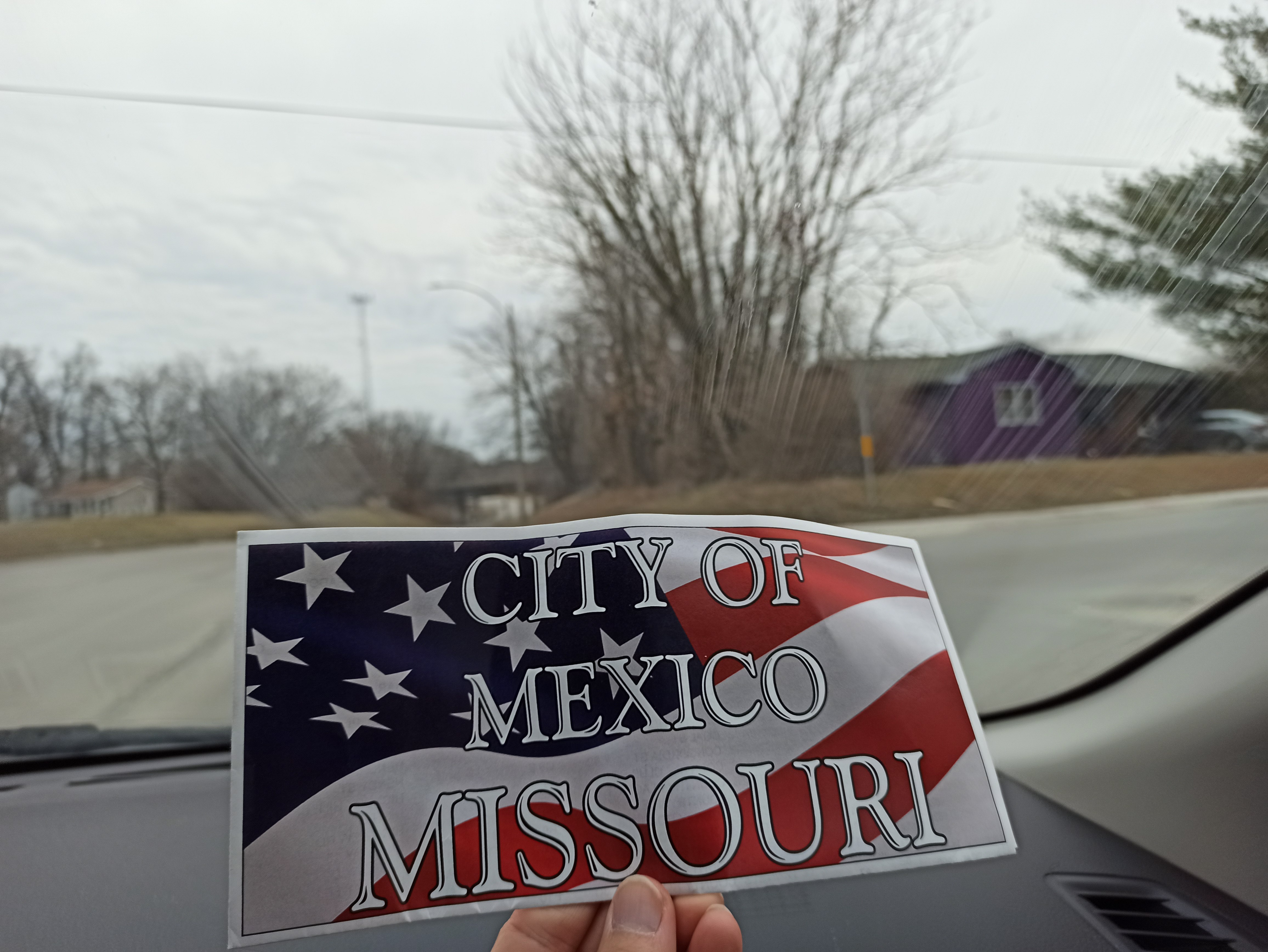 a hand holding a sign in front of a car