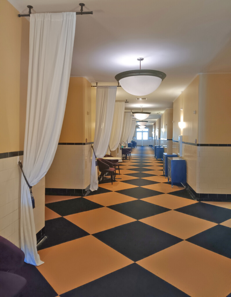 a long hallway with white curtains and black and white checkered floor