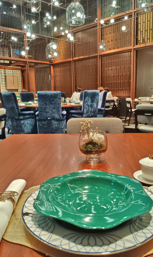 a table with a green plate and a glass vase with a flower in it