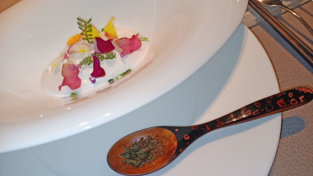 a spoon with a white plate with a white liquid and flowers on it